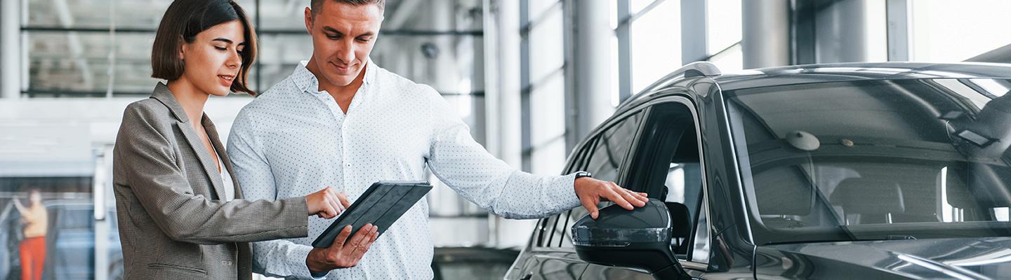 Woman going over details on digital tablet pc with a Man next to car