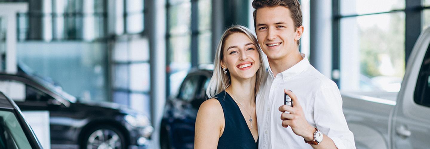 Couple smiling with man holding keys to car in dealership